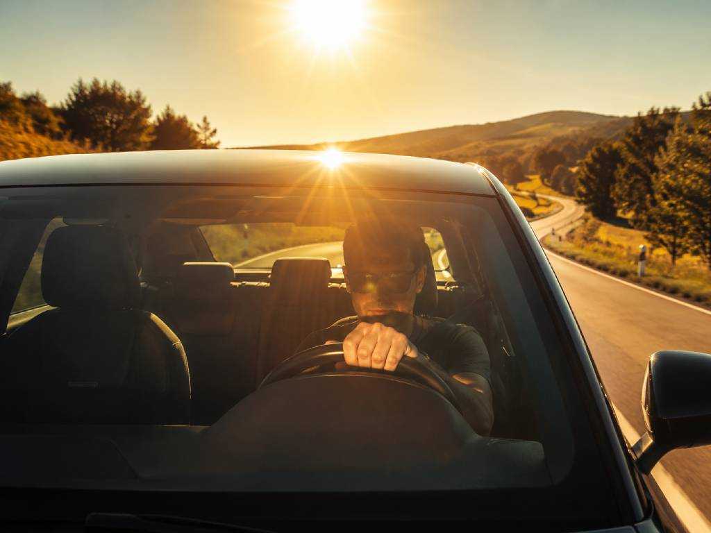 Person fährt bei starker Sonneneinstrahlung im Dienstfahrzeug – UV-Strahlung im Dienstfahrzeug kann Beschäftigte im Außendienst belasten.