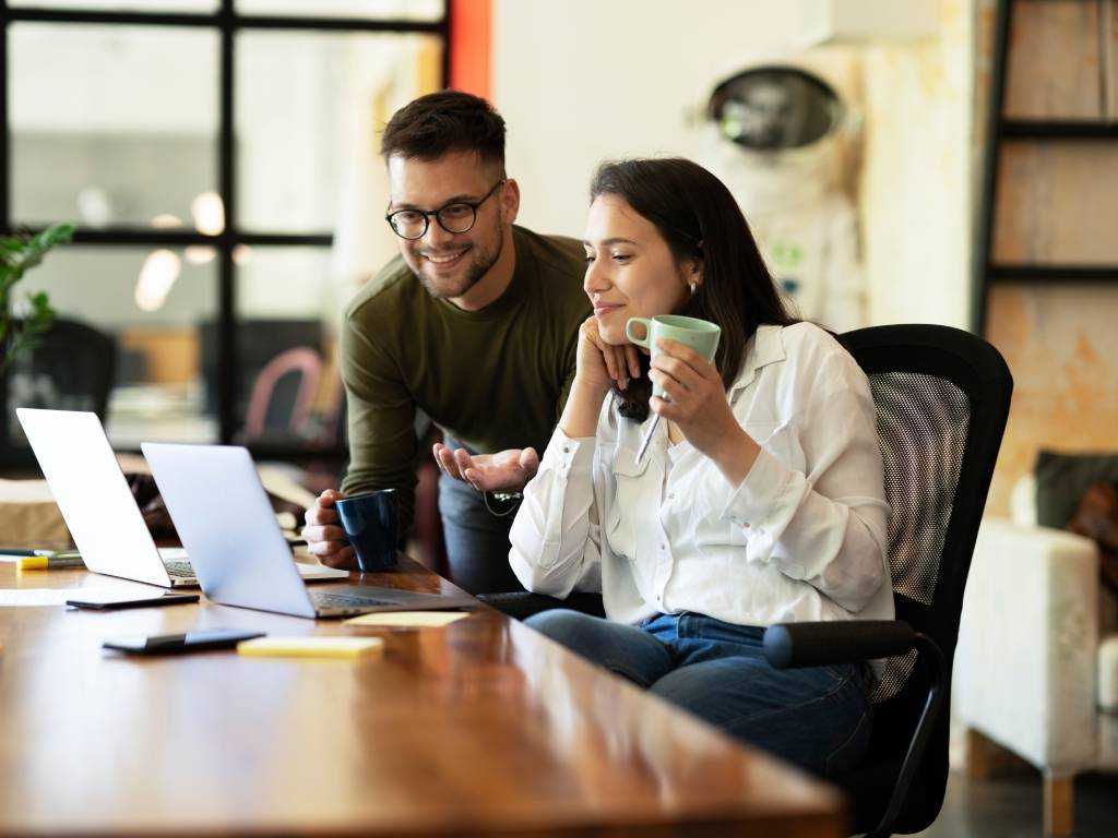 Zwei Personen im Büro trinken Kaffee bei einer Besprechung – symbolisch für Kaffee als Teil des Arbeitsalltags und möglicher Arbeitsunfall