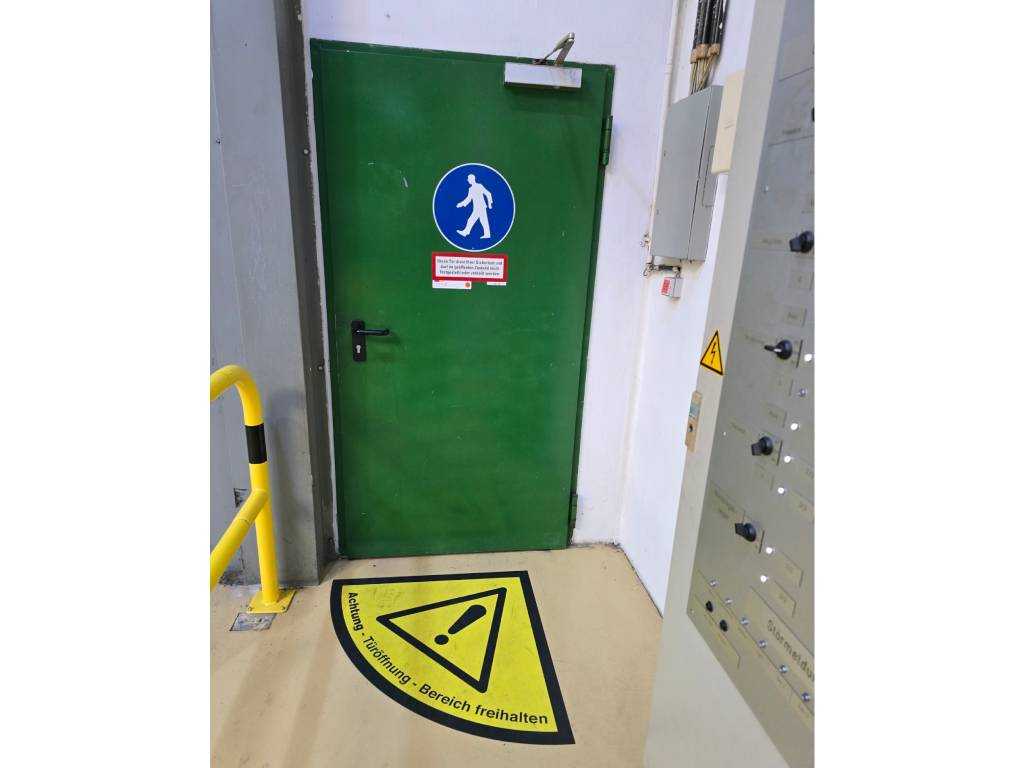 Kennzeichnung von Gefahrenstellen im Betrieb durch Warnzeichen und Bodenmarkierung an einer Tür im Verkehrsweg