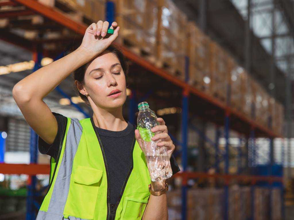 Mitarbeiterin im Lager schwitzt bei Hitze – Hitzeschutz am Arbeitsplatz durch ausreichende Trinkpausen
